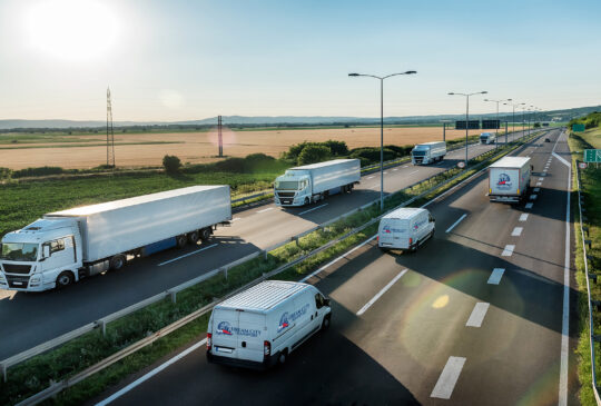 Convoy or caravans of transportation trucks passing vans and truck on a highway on a bright blue day. Highway transit transportation with lorry trucks and vans